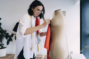Çağdaş atölyede çalışırken mankene iğne batıran ölçüm bandıyla konsantre kadın terzinin yan görünüşü