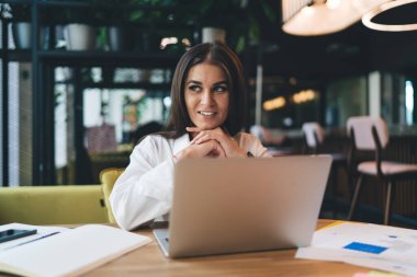 Gündelik giysiler içinde genç ve mutlu bir bayan dizüstü bilgisayar ve defterle oturmuş gülümsüyor ve başka tarafa bakıyordu.
