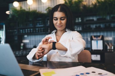 Akıllı, gelişigüzel dokunmatik ekrandaki memnun kadın masadaki bilgisayar ve aydınlık ofisteki belgelerle çalışıyor.