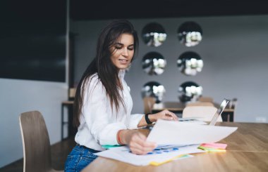 Modern ofiste başarılı bir proje üzerinde çalışan şık giyimli, bilgisayar ve kağıtlı kadın çalışanın yan görünüşü