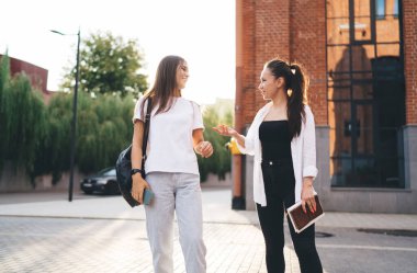 Sırt çantalı, İspanyol sınıf arkadaşıyla sohbet eden hoş bir etnik kız öğrenci. Şehir caddesinde yan yana durup birbirlerine bakıyorlar.