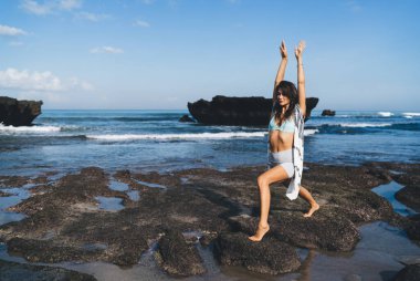 Anjaneyasana 'nın taşlı sahillerinde gün ışığında dalgalanan ve yaz tatilinin keyfini çıkarırken gözlerini kaçıran genç bir kadının vücut tarafı.