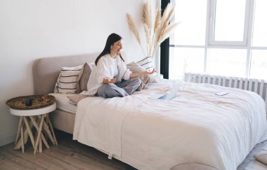 Beyaz tişörtlü ve kulaklıklı genç bir kadın çevrimiçi webinar sırasında konuşurken bacak bacak üstüne atmış bir şekilde oturuyor.