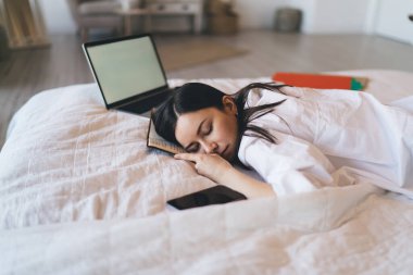 Beyaz tişörtlü, yorgun genç bir kadının hafta sonu kestirirken günlük ve netbook 'la yatağa uzanmasından.