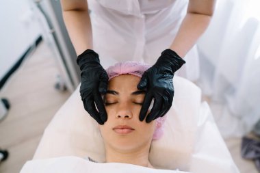 Eldivenli isimsiz bir güzellik uzmanından, sakin bir kadına yüz masajı yaparken, gözleri kapalı yatakta yatarken.