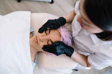 Bulanık eldiven giymiş, masadaki sakin bayanın yüzüne masaj yapan ve ameliyata hazırlanan bulanık ekin güzellik uzmanından.