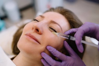 Anonim kozmetik uzmanı güzellik kliniğindeki kadın müşterinin cildindeki kırışıklıkları sıkmak ve düzleştirmek için canlandırıcı yüz enjeksiyonu prosedürü uyguluyor.