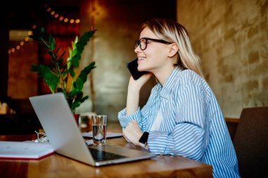 Modern çatı katı tarzı kafede netbook ve proje kağıtlarıyla masada otururken, gözlüklü ve günlük giysiler içindeki kadın girişimcilerin yan görünüşü