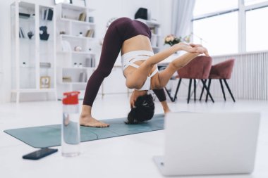 Tanınamayacak kadar zayıf, formda bir kadın, modern odada spor yaparken internetteki antrenman sırasında yoga yapıyor ve vücudunu esnetiyor.