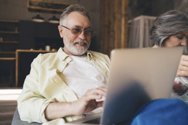 İnternette bilgi ararken ve kanepede otururken günlük kıyafetli, netbook daktilosu kullanan odaklanmış sakallı adam.