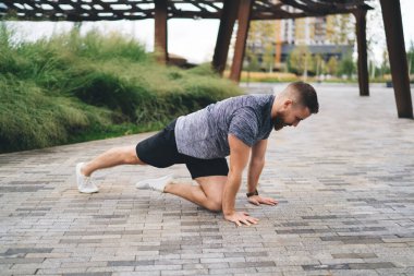 Spor giyimli ve spor ayakkabılı güçlü bir erkeğin parkta spor yaparken bacak esnetme egzersizi yapması.
