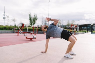 Spor giyim ve spor ayakkabısı giymiş genç bir adamın vücut esneme hareketleri ve spor sahasında spor yaparken yukarı bakması.