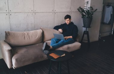 Uzaktan kumandalı erkek konsantrasyon uzmanı. Çağdaş apartman dairesinde koltukta oturup uzaktan bilgisayarla internette sörf yapıyor.