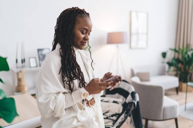 Afro-Amerikan kadın serbest sanatçının, yaratıcı çalışma alanında cep telefonuna göz atan uzun rastalı, akıllı ve serbest çalışanın yan görüntüsü