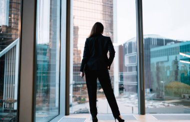 Kendine güvenen, klas siyah takım elbiseli, cebinde koca bir camla duran, kendinden emin genç bir kadın.