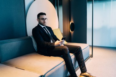 Ofisteki koltukta cep telefonuyla çalışırken ekrana bakıp sörf yapan klas takım elbiseli bir CEO 'nun yan görüntüsü.