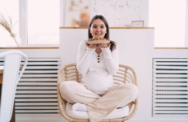 Hafif ev kıyafetleri içinde gülümseyen anne bacak bacak bacak üstüne atmış, rahat hasır koltukta oturmuş lezzetli bir turtayı tatmaya hazır bekliyor.