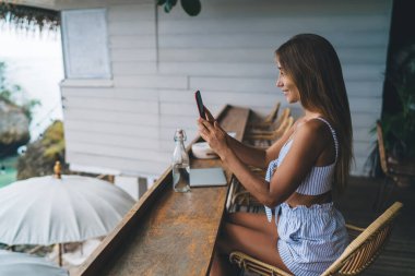 Tayland 'a seyahat ederken, ahşap masada oturan ve açık kafede dinlenen genç bir kadının yan görüntüsü.
