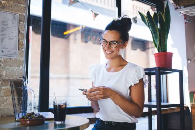 Cep telefonu ve netbook bilgisayar kullanarak gözlük takan mutlu serbest yazarların portresi kameraya gülümserken aynı zamanda iş birliğinde çalışan, cep telefonu ve laptop pozu veren neşeli blogcu.