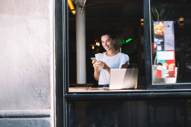 Kameraya gülümseyen dizüstü bilgisayarı ve akıllı telefon cihazları olan neşeli kadın serbest yazar portresi, birlikte çalışırken cep telefonu ve netbook kullanan mutlu Kafkas grafik tasarımcısı ve metin yazarı