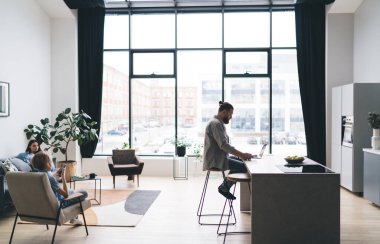 Anne ve oğlu, babamın yanındaki koltukta otururken cep telefonu kullanıyor. Evdeki açık planlama odasındaki pencereye karşı dizüstü bilgisayardaki verileri tarıyor.