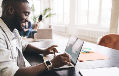 Pozitif Afrika kökenli Amerikalı erkek yöneticinin masada oturması ve başlangıç projesi üzerinde çalışırken dizüstü bilgisayarda yazması yan görünüm