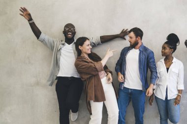 Bir grup çok ırklı iş arkadaşı gri arka planda dikilip eğlenirken Afro-Amerikan kameraya bakıyor ve geriye kalan arkadaşları birbirlerine bakıyor.