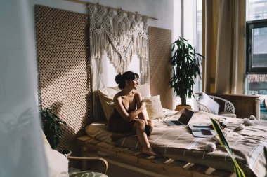 Rahatlamış kadın serbest çalışan, yatak odasındaki uzaktan çalışma sırasında dizüstü bilgisayarın yanında rahat bir şekilde otururken gözlerini kaçırıyor.