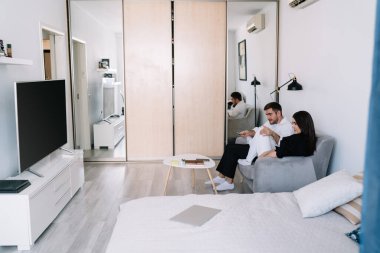 Uzaktan kumandayla oturma odasında televizyon izlerken rahat rahat kanepede dinlenen genç çiftin yan görüntüsü.