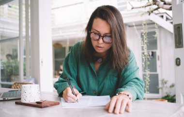 Gözlüklü zeki iş kadını kafeteryada boş zamanlarında rapor belgelerini incelerken, Kafeterya 'nın iç kısımlarında ders yaparken göz düzenleme evrakları hazırlayan Kafkas kadın çalışanı.