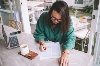 Vizyon koruması için klasik gözlüklü zeki bir kadın Kafe iç planlama üzerinde çalışıyor, modern dizüstü bilgisayarlı Kafkas kadın girişimci belgeleri analiz ediyor