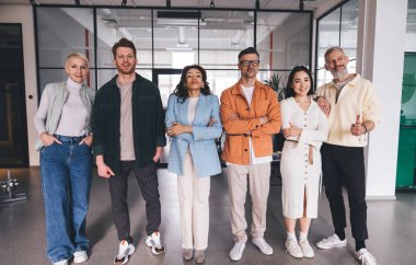 Modern çalışma sahasında cam duvara karşı sıralanmış şık giyinmiş, çok ırklı iş arkadaşlarıyla dolu.