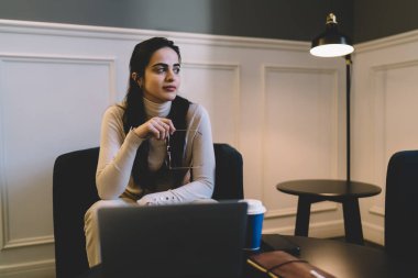 Elinde gözlük olan genç bir bayan serbest yazar dizüstü bilgisayarlı kahve fincanı ile masada otururken gözlerini kaçırıyor ve evde çalışırken dinleniyor.