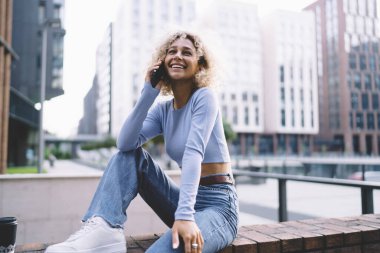 Neşeli siyah kadın gülümsüyor ve yüzünü çeviriyor. Tuğla duvarda elinde kahve fincanıyla oturuyor ve hafta sonu şehir caddesinde cep telefonuyla konuşuyor.