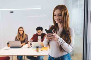 Başarılı bir proje üzerinde çalışırken iş arkadaşlarının karşısında dizüstü bilgisayarlar ve mesajlarla dikilen gündelik kıyafet giyen mutlu kadın ofis çalışanı.