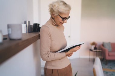 Sıradan giyinmiş ve gözlüklü gülümseyen yaşlı bayanın yan görünüşü rafta duruyor ve evdeki çerçevede hatırlanmaya değer bir resmi izliyor.
