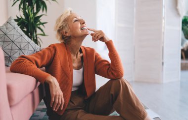 Orta yaşlı, gülümseyen ve koltuğun yanında dinlenen bir kadın. Gözlerini kaçırıp boş zamanlarını evde yalnız geçiriyor.