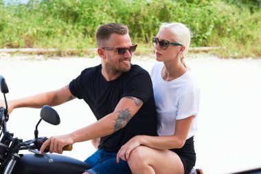 Güneş gözlüklü yakışıklı bisikletçi. Yanında çekici sarışın hippi kızla motosiklet sürüyor. Birlikte seyahat ediyorlar.