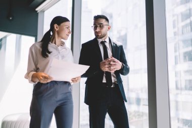 Çağdaş ofis binasında birlikte çalışırken pencerenin yanında duran ve belgeleri kontrol eden konsantre iş arkadaşlarının düşük açısı