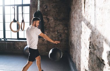 Spor kıyafetleri içinde sportif bir adamın spor salonunda atım antrenmanı yaparken spor topuyla egzersiz yapması.