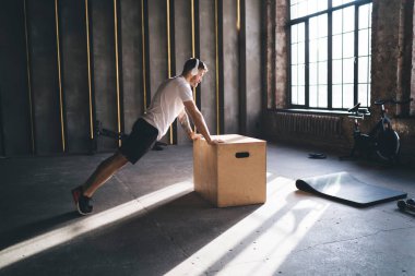 Spor giyim ve kulaklıklarda odaklanmış bir erkek sporcunun modern ferah fitness kulübünde atlama kutusu üzerine basın egzersizi yaparken müzik dinlemesi.
