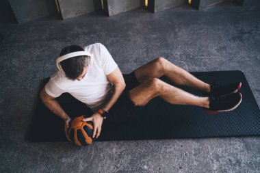 Spor kıyafetleri ve kablosuz kulaklıklar takan güçlü erkek sporcuların spor salonunda antrenman yaparken abdominal mekik çekmesinden.