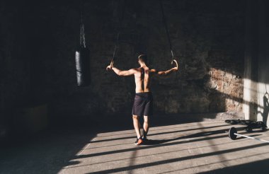Beden eğitiminde akrobatik egzersize hazırlanırken kolları bantlı, güçlü üstsüz, tanınmayan erkek sporcunun arka planda duruşu.