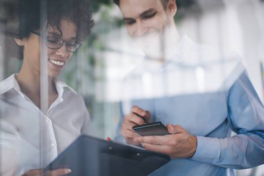 İş kadını, erkek arkadaşı akıllı telefon kullanırken panoya yazı yazıyor. İş birliği ve takım çalışması kavramı. Genç Kafkasyalı bin yıllık meslektaşlar görev başında. Modern başarılı insanlar