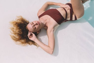 Kırmızı mayo giyen genç ve şehvetli bir kadının yazın dinlenirken yere uzanmış saçlarına dokunuşunun en üst görüntüsü.