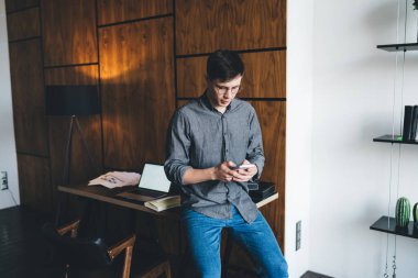 Evde yaratıcı çalışma alanı projesinde çalışırken ara verildiğinde masada dizüstü bilgisayarlı ve akıllı telefonları karıştıran meşgul genç adam.