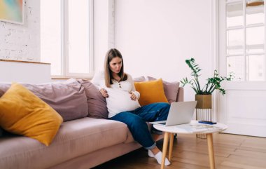 Dizüstü bilgisayarda doğum kursuna katılan genç bir kadının tüm vücudu koltukta oturup nefes alma egzersizi yaparken tekmelendiğini hissediyor.