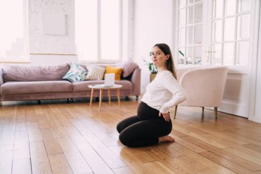 Uzunca bir süre sakin bir kadın bebek bekliyor. Elleri belinde oturuyor. Geniş salonda spor yaparken kameraya bakıyor.