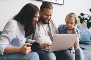 Mutlu bir aile, gündelik kıyafetleriyle kanepede dinlenirken bilgisayardaki eski fotoğrafları izliyorlar. Geçen hafta sonunu birlikte geçirdiğimiz zamanları anımsıyorlar.