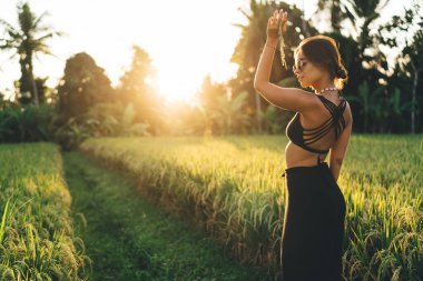Güneş gözlüklü genç bayan turistin çim tarlasında dikilirken elinde pirinçle paniklediğini ve yazın gün doğumunda gözlerini kaçırdığını görüyoruz.